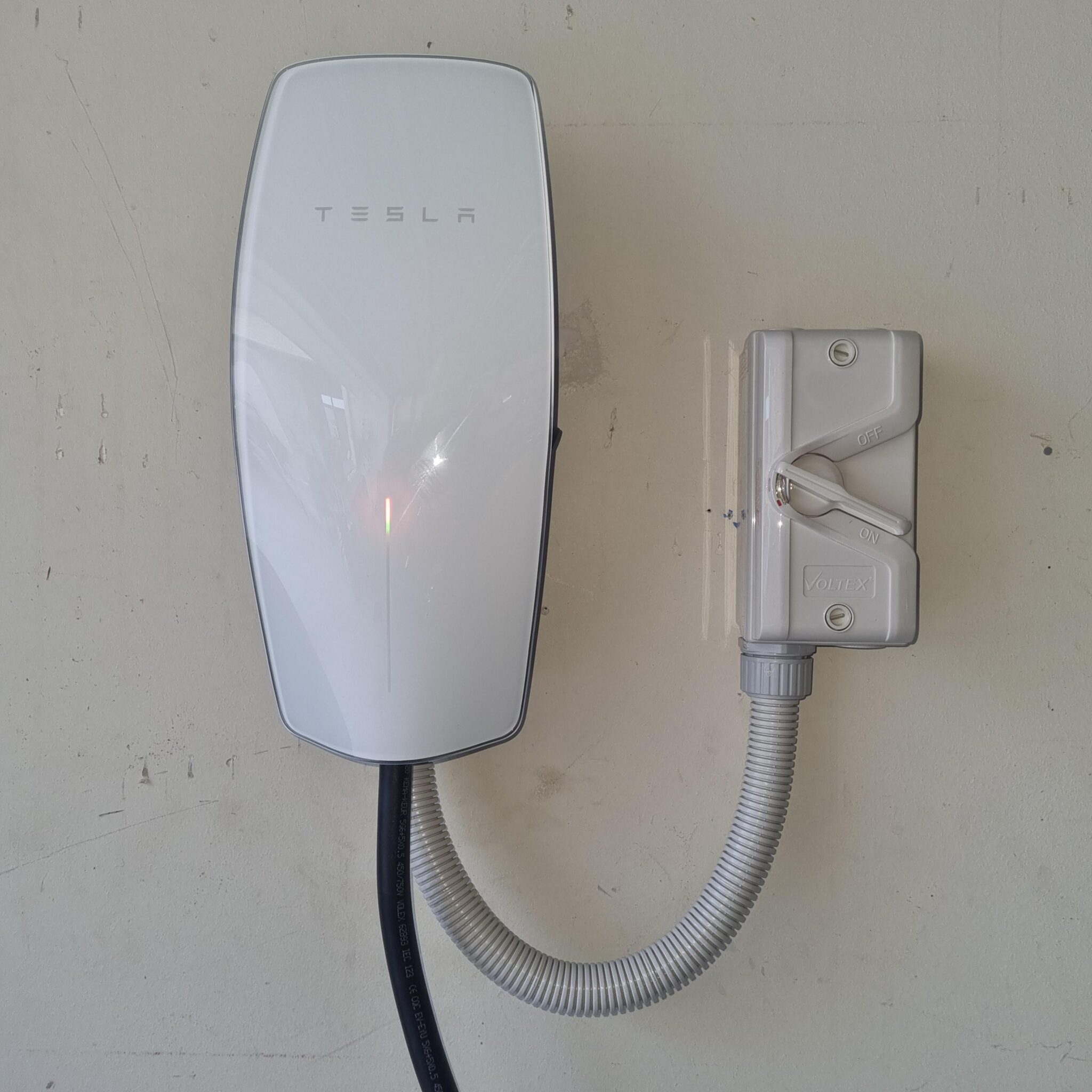 Tesla wall connector mounted on a wall with a cable management system attached.